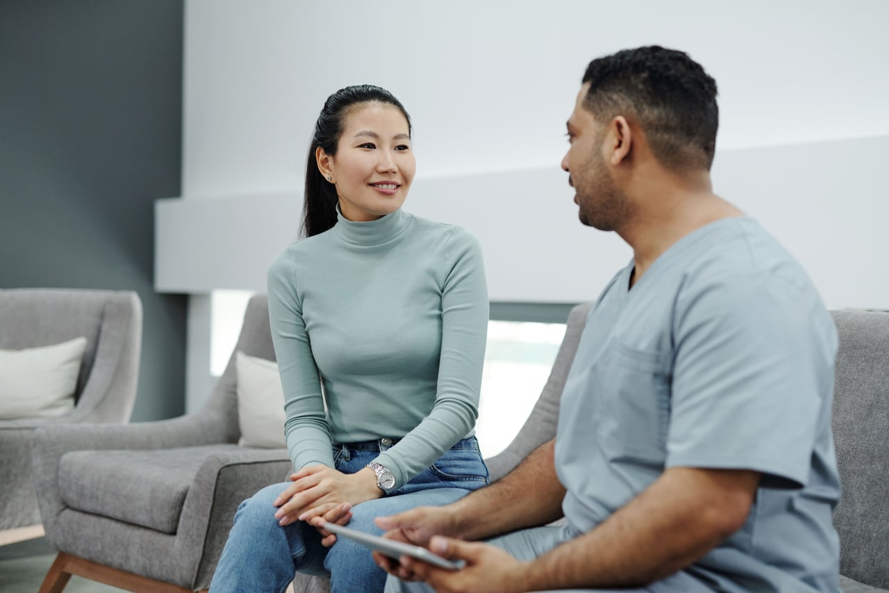 A seated woman speaking with a clinician holding a tablet.